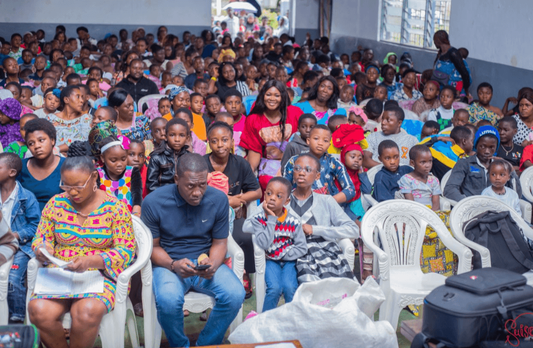 A packed hall of children and families at a Back to School event in Cameroon, with TMTF founder Dorothy Akoh-Arrey standing among them